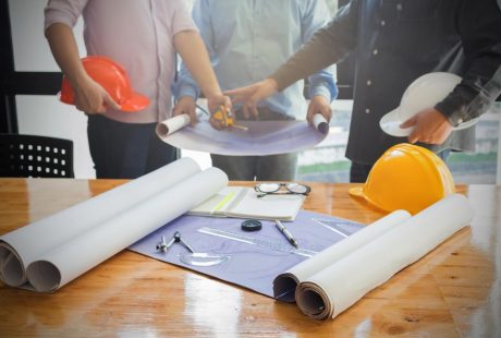 Contractors with plans, measuring tools, and hardhats having a discussion